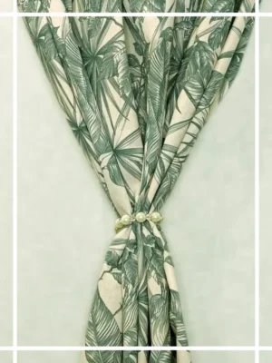 Green tropical leaf print curtain fabric on neutral base with pearl tieback, botanical palm pattern drapes for modern interiors.