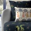 Dark floral upholstered armchair with vintage botanical fabric and decorative cushion featuring traditional folk art women illustration in an elegant living room setting