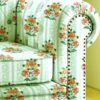Vintage floral sofa upholstery fabric in pastel green with orange and yellow flower motifs, striped pattern, and classic rolled arm sofa design for elegant living room interiors.