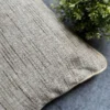 Luxury beige textured cushion upholstery fabric with subtle linear weave, styled on a grey surface with greenery for premium modern interiors