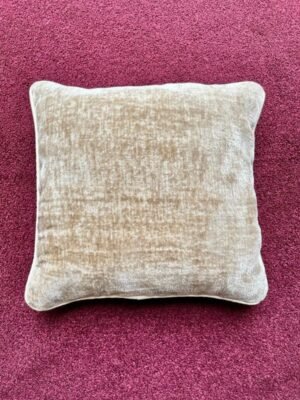 Luxury neutral beige velvet cushion cover with soft textured upholstery fabric, styled on a rich burgundy carpet for premium interior décor.