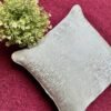 Luxury textured cushion cover fabric in soft pearl silver with subtle metallic sheen, styled on a rich burgundy surface for premium modern interiors.