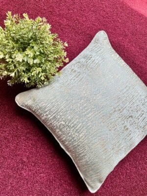 Luxury textured cushion cover fabric in soft pearl silver with subtle metallic sheen, styled on a rich burgundy surface for premium modern interiors.