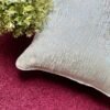 Luxury textured cushion cover fabric in soft pearl silver with subtle metallic sheen, styled on a rich burgundy surface for premium modern interiors.