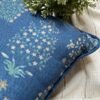 Luxury blue floral cushion cover fabric with delicate botanical motifs in soft green and beige, styled on neutral bedding for premium interior décor.