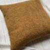 Luxury caramel bouclé cushion cover fabric with rich textured upholstery, styled on neutral bedding for premium interior décor.