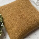 Luxury caramel bouclé cushion cover fabric with rich textured upholstery, styled on neutral bedding for premium interior décor.