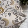 Luxury floral designer fabric in beige with mustard and grey botanical motifs, used for bespoke cushion covers styled on a modern premium bedroom setting.