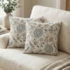 Luxury cream cushion covers with elegant blue floral and vine pattern in premium woven fabric, styled for sophisticated living room and bedroom interiors.