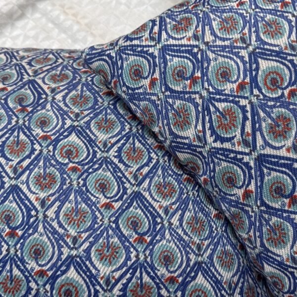 Luxury blue geometric patterned designer cushion with intricate swirl motifs styled on textured wallpaper background, premium interior decor inspiration.