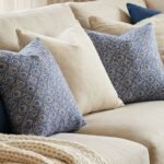 Luxury blue geometric patterned designer cushion with intricate swirl motifs styled on textured wallpaper background, premium interior decor inspiration.
