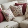 Luxury floral cushion cover in beige woven fabric with pink, burgundy and blue botanical pattern, premium soft furnishing accent for elegant living room and bedroom interiors.