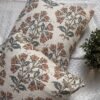 Premium designer cushion covers in beige cotton fabric featuring hand-block style rust floral motifs with sage green leaves, styled for luxury living room and bedroom interiors.