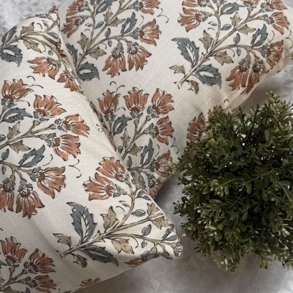 Premium designer cushion covers in beige cotton fabric featuring hand-block style rust floral motifs with sage green leaves, styled for luxury living room and bedroom interiors.