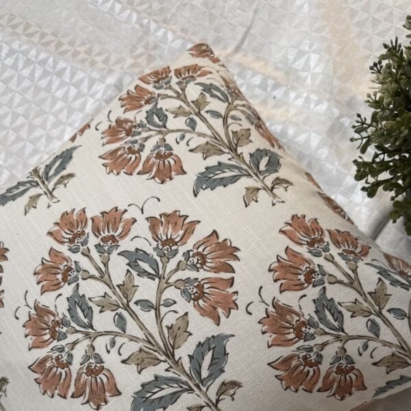 Premium designer cushion covers in beige cotton fabric featuring hand-block style rust floral motifs with sage green leaves, styled for luxury living room and bedroom interiors.