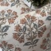 Premium designer cushion covers in beige cotton fabric featuring hand-block style rust floral motifs with sage green leaves, styled for luxury living room and bedroom interiors.