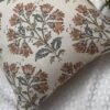 Premium designer cushion covers in beige cotton fabric featuring hand-block style rust floral motifs with sage green leaves, styled for luxury living room and bedroom interiors.
