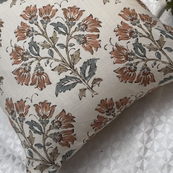 Premium designer cushion covers in beige cotton fabric featuring hand-block style rust floral motifs with sage green leaves, styled for luxury living room and bedroom interiors.