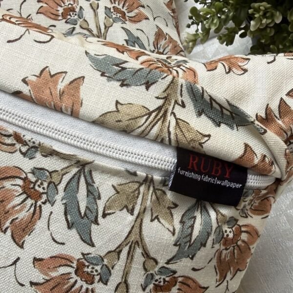 Premium designer cushion covers in beige cotton fabric featuring hand-block style rust floral motifs with sage green leaves, styled for luxury living room and bedroom interiors.