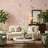 Soft blush pink floral mural wallpaper with delicate white botanical branches and birds, styled in a modern luxury living room with a grey sofa and glass coffee table