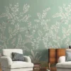 Elegant sage green floral mural wallpaper with white botanical branches and birds in a modern living room with teal sofa, wooden accents, and neutral décor