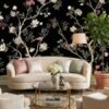 Daisy Bennett mural wallpaper by RUBY featuring delicate floral trees with blossoms and birds on a black background, styled in a modern luxury living room with a white sofa and soft decor