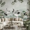 Luxury neutral grey mural wallpaper featuring elegant cranes, lotus flowers, and botanical branches in a serene landscape design, styled in a modern living room with beige sofa and green armchairs by RUBY Furnishing Studio Ghatkopar East Mumbai.