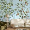 Botanical mural wallpaper featuring citrus trees with oranges and lemons on a soft blue background, styled in a modern living room with a curved cream sofa, green velvet chair, and natural textures.