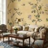 Warm yellow floral bird mural wallpaper with delicate blossoms, citrus accents, and birds, elegant botanical wall design in a luxury bedroom setting with soft pink seating.