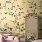 Warm yellow floral bird mural wallpaper with delicate blossoms, citrus accents, and birds, elegant botanical wall design in a luxury bedroom setting with soft pink seating.